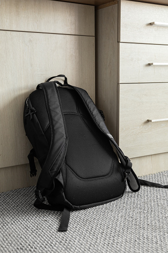 black fabric backpack with straps on a carpet and leaning against a desk, texture detail