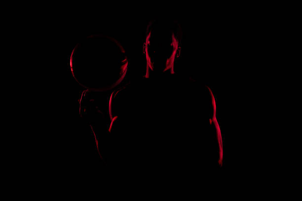 giocatore di basket che gira una palla su sfondo nero. uomo afroamericano rosso lato illuminato silhouette - streetball basketball sport men foto e immagini stock