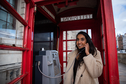 Girl makes a phone call inside a red telephone box in London. Beautiful smiling and attractive woman on the phone