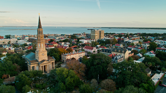 Aerial shot of Charleston, South Carolina at sunset, looking past the spire of St Philip's Church towards the harbor.