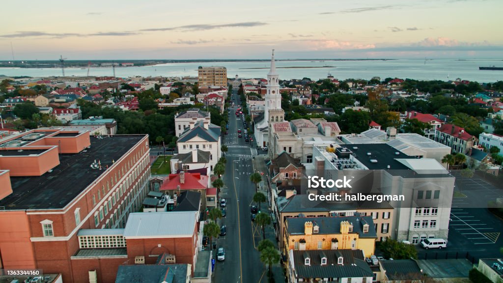 Drone Flight Over Broad Street in Charleston, South Carolina at Sunset Aerial shot of Charleston, South Carolina at sunset, flying over the church spires and the rooftops of colonial style houses in the Harleston Village neighborhood towards the harbor. Charleston - South Carolina Stock Photo