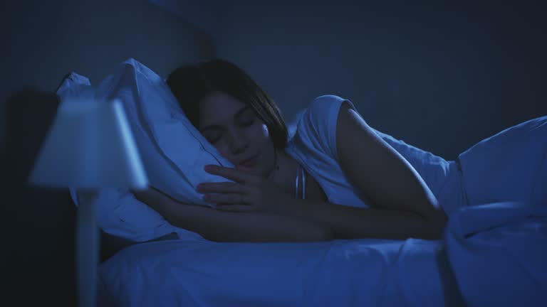 An young brunette woman is switching off the light and going to sleep peacefully under warm duvet blanket in a cosy bed in a bedroom. Concept of comfort, relax,sleeping,health,bedding,softness,dreams