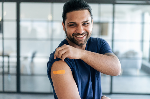 Portrait of man showing hir arm with band aid after coronavirus Covid-19 vaccine injection