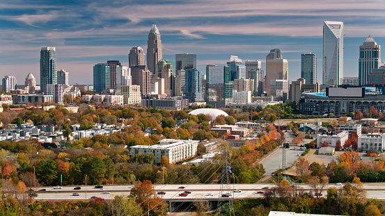 Drone shot of Charlotte, North Carolina on a Fall afternoon, looking over autumnal trees and a busy freeway towards the Uptown skyline.   \n\nAuthorization was obtained from the FAA for this operation in restricted airspace.