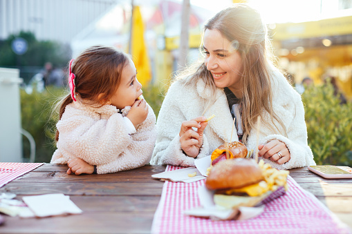 Mather and daughter at fast food restaurant. They're eating burgers and hot dog