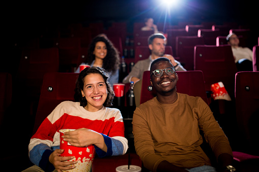 Girl watching a comedy movie at the cinema with her African American friend.