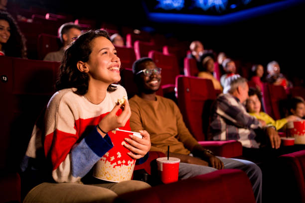 Friends enjoying a comedy movie at the cinema Girl watching a comedy movie at the cinema with her African American friend. spectator stock pictures, royalty-free photos & images
