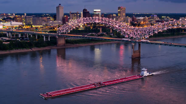 istock Mississippi River Barge Passing Memphis on Stormy Evening Under Illuminated Hernando de Soto Bridge - Aerial 1363353445