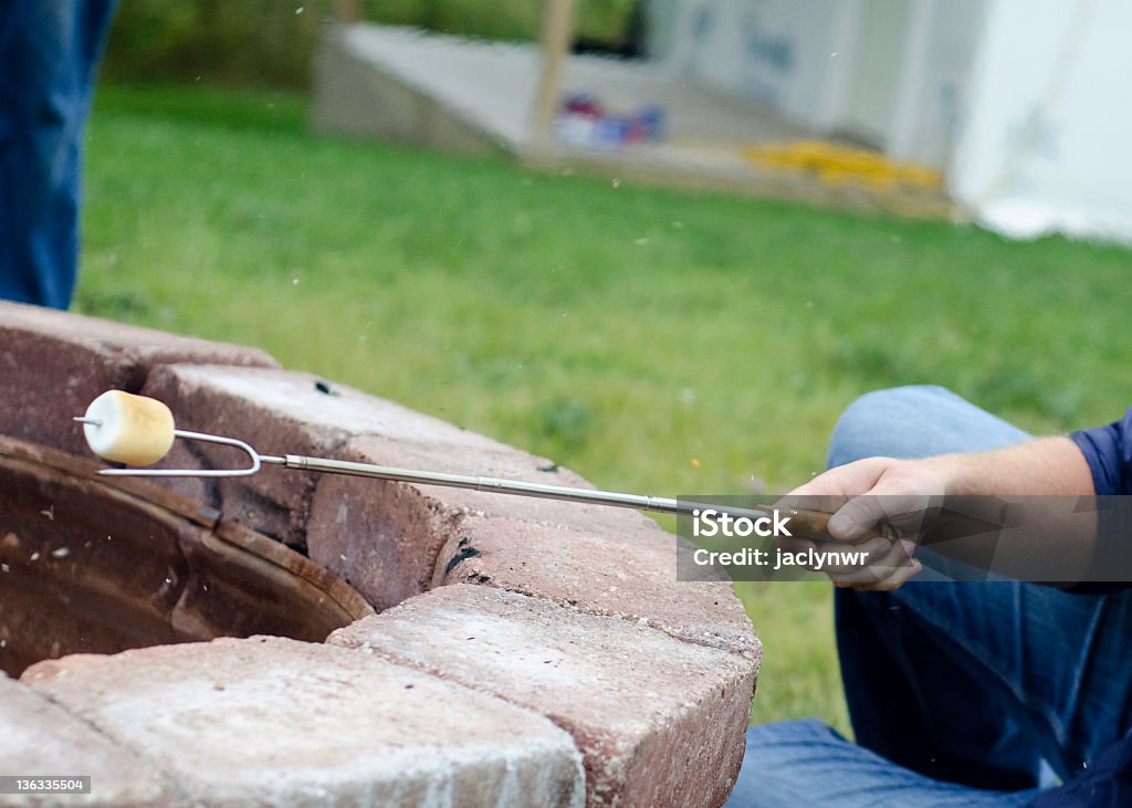 roasting a marshmallow over the fire a man roasting a marshmallow over a fire pit Fire - Natural Phenomenon Stock Photo