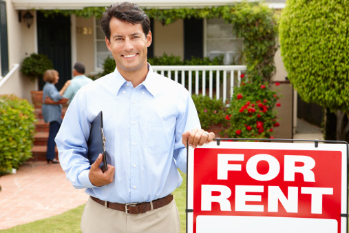 Real estate agent at work standing next to 'for rent' sign