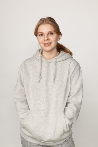 Studio portrait of attractive 18 year old blonde woman in gray hooded shirt on white background