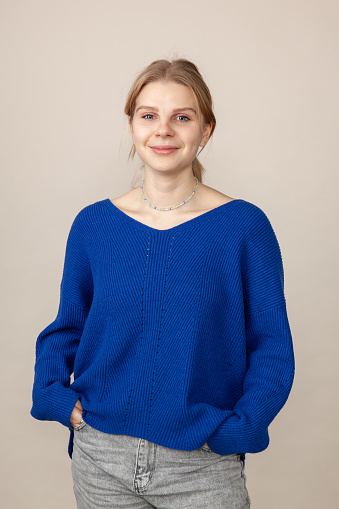 Studio portrait of attractive 18 year old blonde woman in blue sweater on beige background