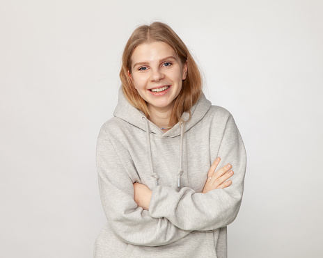 Close-up studio portrait of attractive 18 year old blonde woman with long hair in gray hooded shirt on white background