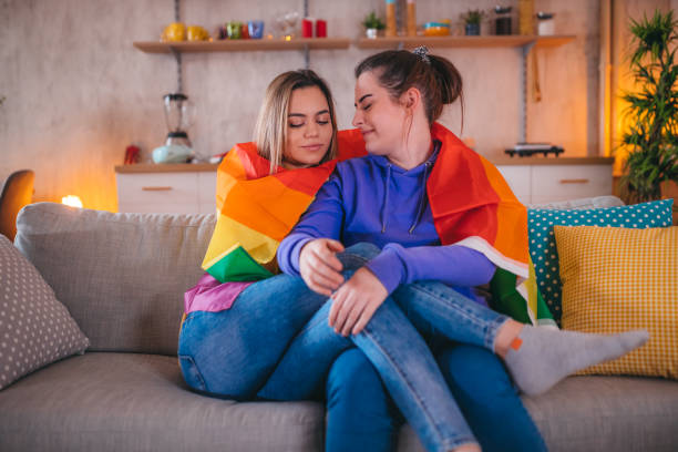 istock Young lesbian couple embracing on sofa with rainbow flag 1363359816