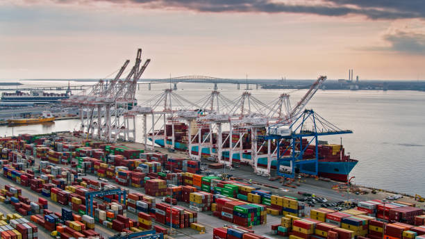 Loading Container Ship in the Port of Baltimore - Aerial Aerial shot of the Port of Baltimore at sunset, looking across and intermodal container yard towards a ship being loaded by cranes. In the distance, the Key Bridge stretches across the river. commercial dock stock pictures, royalty-free photos & images