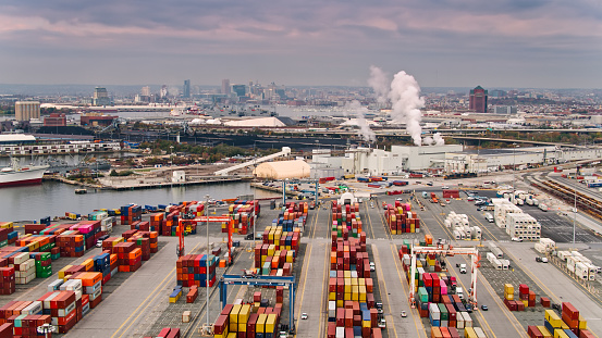 Aerial shot of the Port of Baltimore at sunset, looking across a container terminal and over industrial facilities along the quayside towards the city skyline.