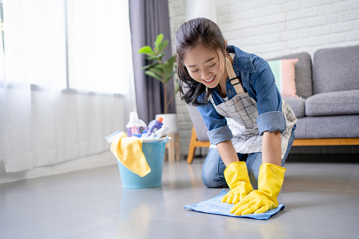 Smiling beautiful Asian woman washes the floor with a yellow rag and detergent.