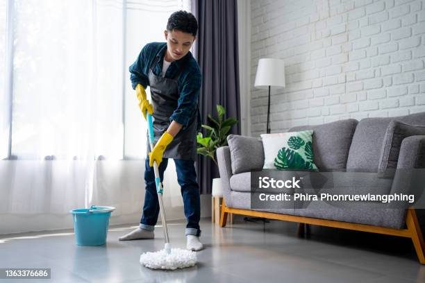 Handsome Asian Man Wearing Apron Cleaning Floor At Home Guy Washing Floor With Mopping Stick And Bucket In Living Room Stock Photo - Download Image Now
