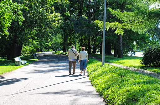 An elderly couple walks close to each other along the empty Yelagin alley in St. Petersburg park.