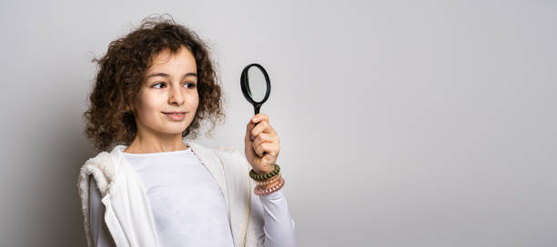 one small caucasian girl ten years old with curly hair front view portrait close up standing in front of white background looking to the camera holding magnifying lens education and learning concept - magnifying glass lens holding europe imagens e fotografias de stock