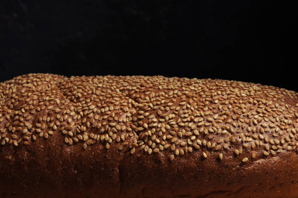 istock Bread crust is sprinkled with sesame seeds, light on top, black background.Dark food. 1363399723