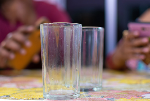Empty glass standing on the wooden table. Man and woman sitting and surfing phone on background. Selective focus.