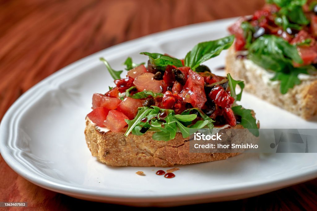 Bruschetta with sun-dried tomatoes and feta in a white plate on a wooden background Canape Stock Photo
