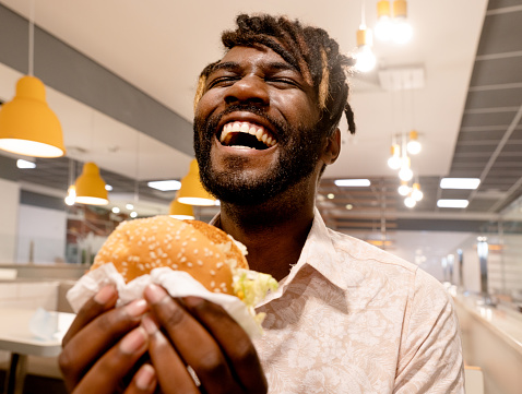 Close-up of a young man enjoying having burger while sitting inside a restaurant