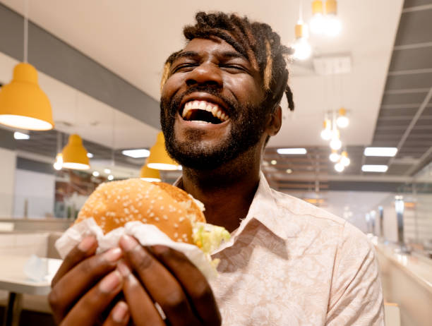 young man enjoying having burger at a restaurant - burger hamburger large food imagens e fotografias de stock