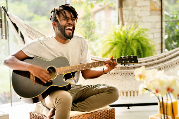 smiling young man playing an acoustic guitar - men artist guitarist guitar imagens e fotografias de stock