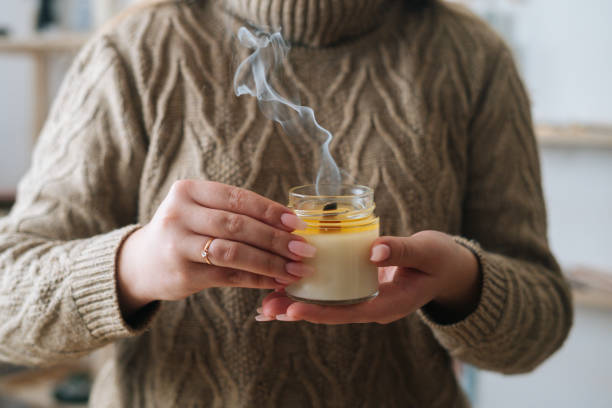 plan rapproché d’une jeune femme méconnaissable tenant une bougie éteinte faite à la main dans un bocal en verre près de la poitrine. - bougie mains photos et images de collection