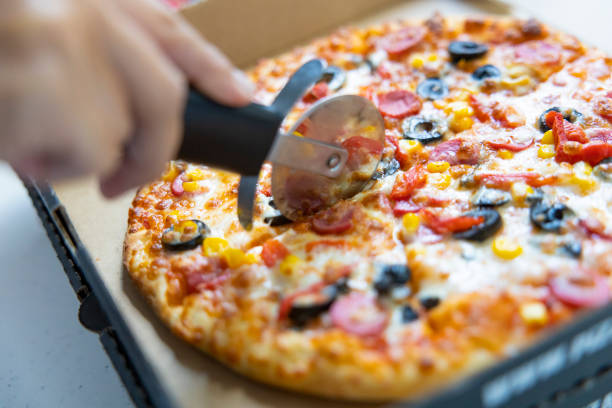Young woman cutting pizza on cardboard box