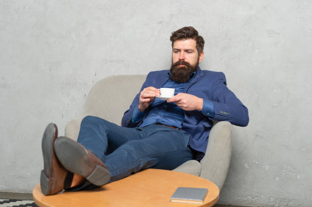 brodaty facet w garniturze pij herbatę lub kawę relaksując stopy w fotelu wypoczynkowym podczas przerwy w pracy, zrelaksuj się - content businessman executive director manager zdjęcia i obrazy z banku zdjęć