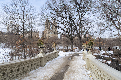 New York City, New York, United States - February 14, 2021: Central Park and Bow bridge in the winter, after a snow storm. View of upper west side buildings.
