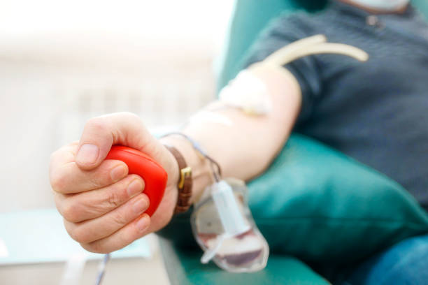 Topic of donation. Man donates blood in hospital. Man's hand squeezes rubber heart. Close-up. Donor sits in chair Topic of donation. Man donates blood in hospital. Man's hand squeezes rubber heart. Close-up. Donor sits in chair. Background. blood test stock pictures, royalty-free photos & images