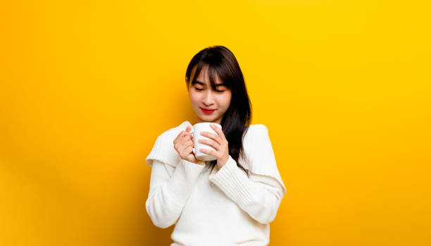 image of young woman having fun enjoying coffee cup at home smiling beautiful girl drinking hot tea in winter and smiling happily on yellow background. - coffee time restaurant imagens e fotografias de stock