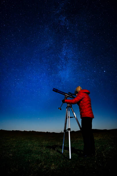 In touch with reality Woman with refracting telescope pointing towards an object in the sky on a moonlit night. The night sky shows the plane of the galaxy near the summer triangle of Altair, Deneb and Vega. looking through an object stock pictures, royalty-free photos & images