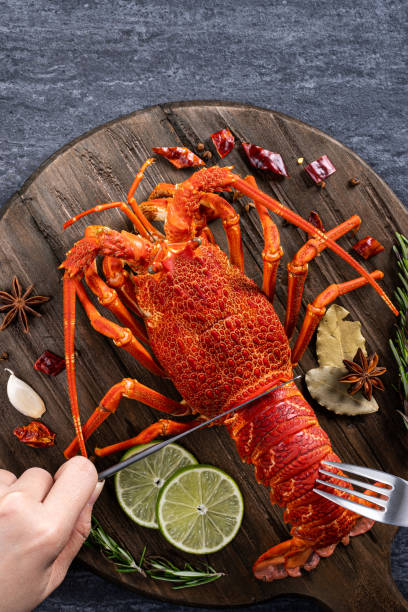 Cooked lobster with spices for valentine's day meal. Top view of cooked boiled lobster, delicious dinner seafood meal set with knife and fork on black stone slate background for Valentine's day concept. food state preparation shrimp prepared shrimp stock pictures, royalty-free photos & images