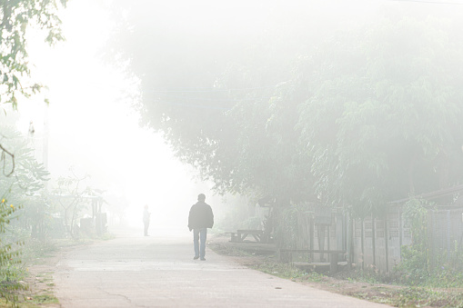 Man walking alone  in the fog in winter in a street in rural Asia
