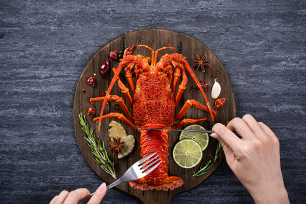 Cooked lobster with spices for valentine's day meal. Top view of cooked boiled lobster, delicious dinner seafood meal set with knife and fork on black stone slate background for Valentine's day concept. food state preparation shrimp prepared shrimp stock pictures, royalty-free photos & images