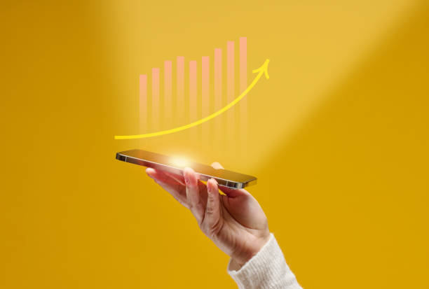 istock female hand holds a smartphone with holographic graphics on a yellow background. Performance growth, success 1363435527