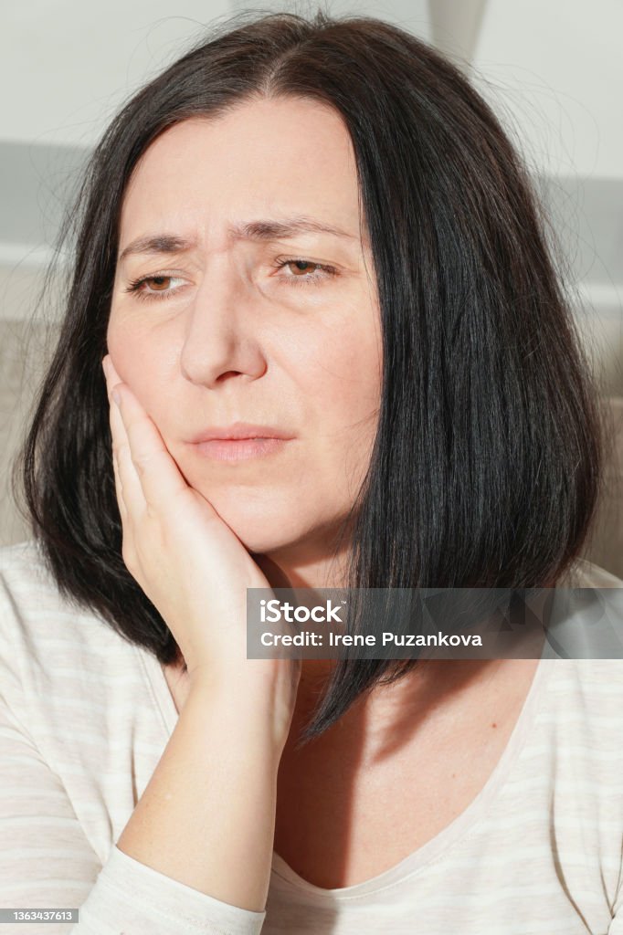 Middle age mature woman touching mouth with hand suffering from toothache at home. Dental health concept. Tooth decay, inflammation or sensitive teeth. 40-44 Years Stock Photo