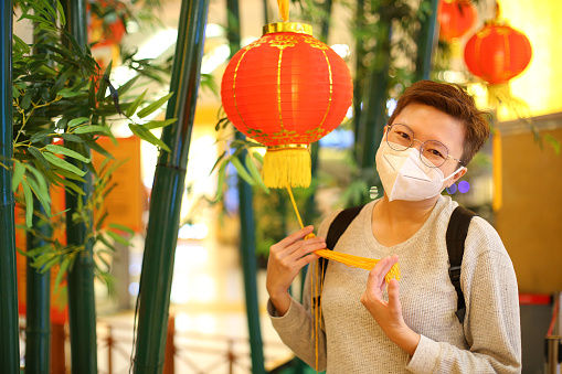 An Asian woman is feeling cheerful with Chinese New Year decorations -  self portrait with Chinese lantern hanging at bamboo tree.