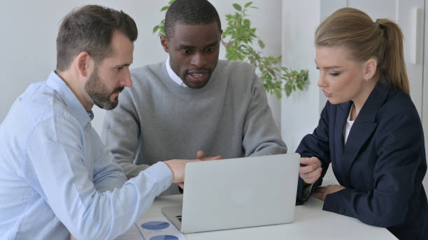 istock Mixed Race Business People having Serious Discussion while using Laptop in Office 1363441305