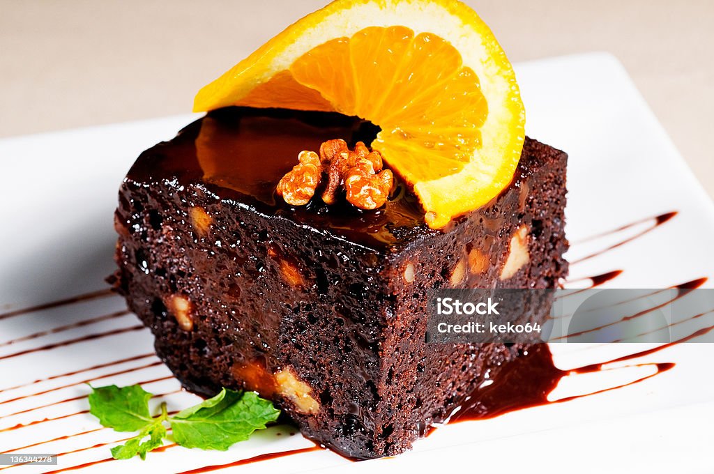 chocolate and walnuts cake fresh baked delicious chocolate and walnuts cake with slice of orance on top and mint leaf Baked Stock Photo