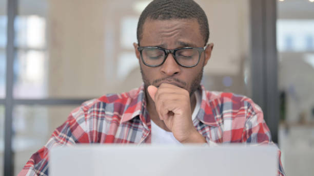 istock Close Up of African Man Coughing while using Laptop 1363443548
