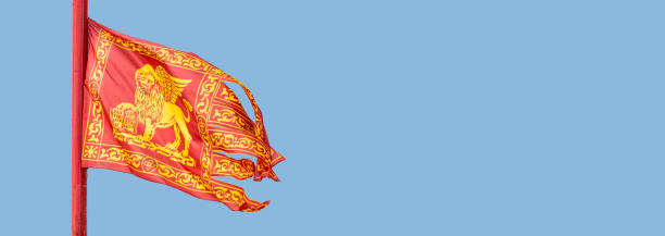 Banner with an old traditional city flag of Venice, Italy, depicting Venetian lion with wings and Bible at blue sky background with copy space. stock photo