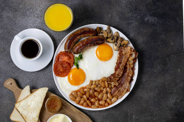 Full english breakfast with fried eggs, sausage, mushrooms, beans, toast and coffee on a dark background, top view Full english breakfast with fried eggs, sausage, mushrooms, beans, toast and coffee on a dark background, top view english breakfast stock pictures, royalty-free photos & images
