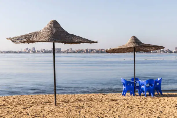 Photo of Umbrellas and blue plastic chairs are on the beach at Lake Timsah