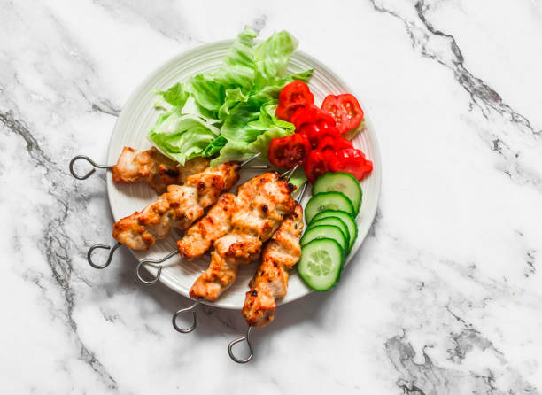 Peanut butter, yogurt and soy sauce chicken satay skewers with fresh vegetables salad on a light background, top view. Delicious tapas